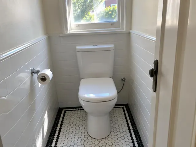 Clean white toilet in a small tiled bathroom with a window and patterned floor in North Sydney
