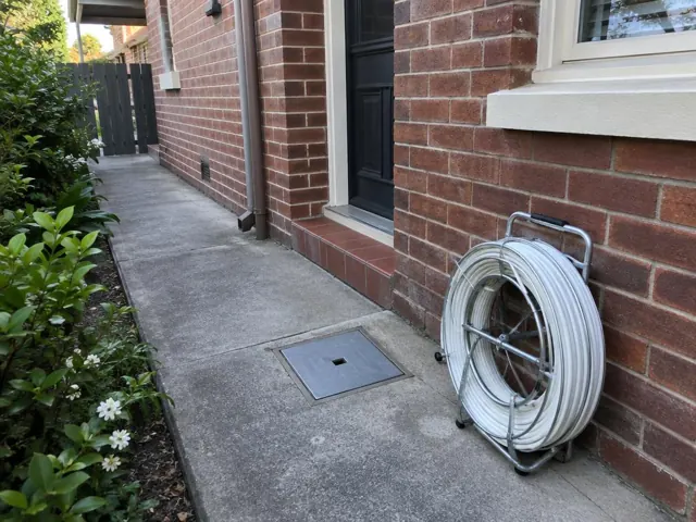 Capped square access point in a concrete side path beside a brick house in Waverton
