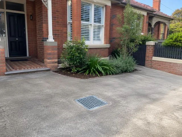 Flush stormwater grate in a concrete driveway beside a brick house and garden in Crows Nest