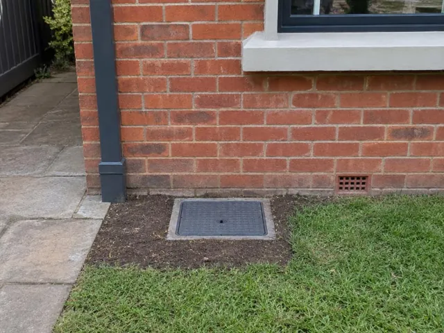 Capped sewer opening set in tidy soil beside a brick house wall in North Sydney